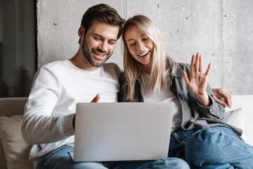 Poster - Happy young couple gesturing and using laptop while sitting on couch