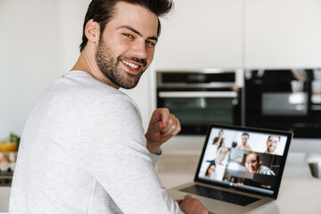 Wall Mural - Joyful unshaven man smiling while taking conference call on his laptop