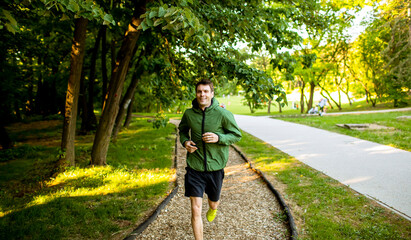 Athletic young man running while doing workout in sunny green park