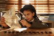 © New Africa - Cute little detective exploring document with magnifying glass at table in office