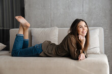 Happy Brunette Nice Girl Smiling While Lying On Sofa At Home