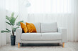 © Julia - Gray sofa with yellow pillow simple living room. modern living room with cozy sofa and flower in a pot - palm tree, background large light windows and curtains