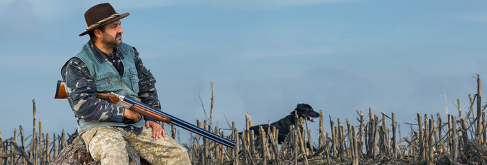 A hunter with a gun in his hands in hunting clothes in the autumn forest in search of a trophy. A man stands with weapons and hunting dogs tracking down the game.