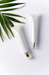 Two tubes for cream lie on a white background with a palm leaf