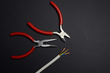 Wall Mural - wire cutters, pliers and stripped wire lie against a dark background. close-up.