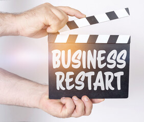 On a white background, a man holds a clapperboard in his hands on which it is written - BUSINESS RESTART