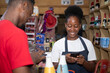 © Confidence - shop attendant accepting mobile fund transfer as payment from a customer