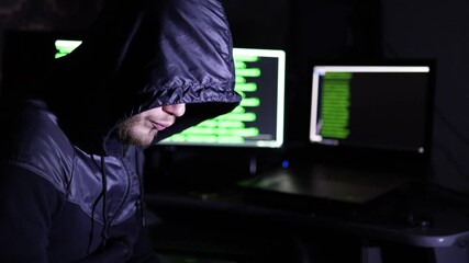 Male hacker cybercriminal in a hood sits at the computer. Internet crime concept