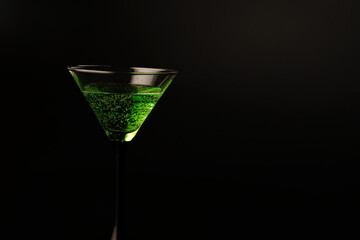 Two glasses with a green cocktail on a black background. One glass is full and the other is empty