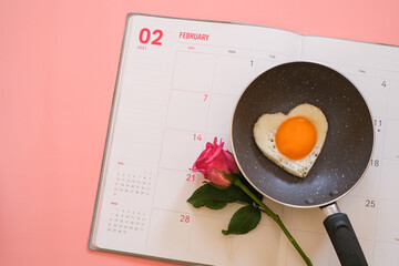 Wall Mural - Heart shape fried egg in the pan and pink rose on the calendar isolated on pink background. top view. Valentine's day concept.  Copy space for text 