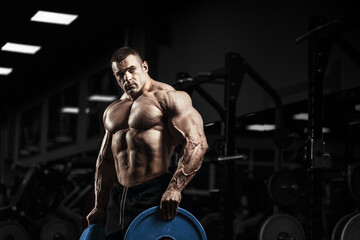 Wall Mural - Muscular man bodybuilder training in gym and posing. Fit muscle guy workout with weights and barbell
