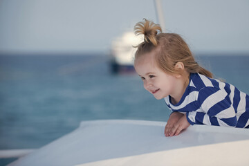 Wall Mural - Child with happy smiling face. Family summer vacations and journey. Childhood and happiness concept. Adorable kid in striped blue and white shirt on boat. Yachting and sailing along sea.