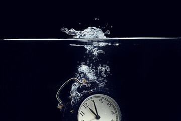 Alarm clock falling into the water against black background