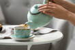 © Pixel-Shot - Woman pouring tea from teapot into cup on table in room