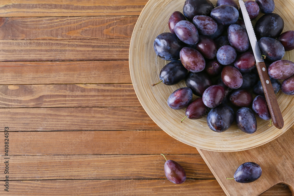 Plate with tasty plums on wooden background
