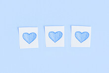 Three Blue Hearts Drawn In Pencil On Pieces Of White Paper On A Blue Background.