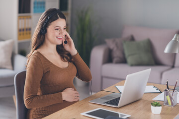 Poster - Photo of pregnant customer support adviser sit table hand belly wear headset brown shirt workstation office indoors