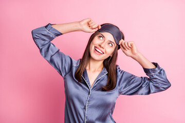 Sticker - Photo portrait of dreamy girl touching sleeping mask with two hands looking up isolated on pastel pink colored background