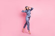 Full length body size photo of brunette in blue pajama jumping smiling touching sleeping mask isolated on pastel pink color background