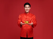 © NaMong Productions - Happy Chinese new year. Asian man wearing in traditional costume holding gold ingot isolated on red background.