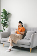 Girl With Earphones Listening To Music On Mobile Phone Sitting On A Couch