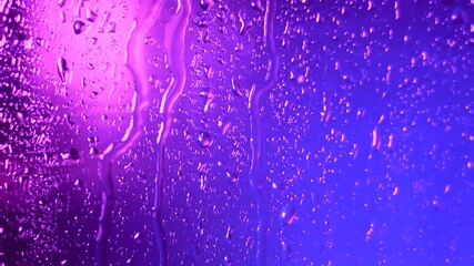raindrops of water flow down the glass in rainy weather on a colored pink blue blurred background. t