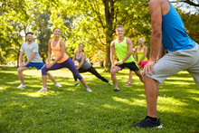 Fitness, Sport And Healthy Lifestyle Concept - Group Of Happy People Exercising With Trainer At Summer Park