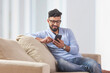 © IndiaPix - Young man sitting on the couch and using his mobile.