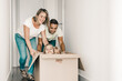© Mangostar - Happy Caucasian parents playing with children sitting in carton box at new home. Joyful family enjoying new house. Mom, dad and daughters having fun during removal. Relocation and moving day concept