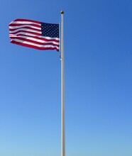 Low Angle View Of American Flag Waving Against Blue Sky