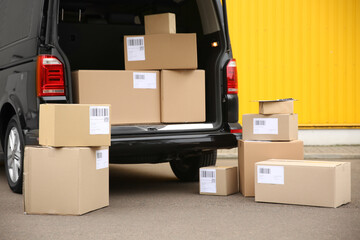 Canvas Print - Black delivery van and many different parcels near yellow wall outdoors. Courier service