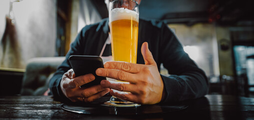 Wall Mural - close up of man hand hold smartphone, drinking beer and reading message at bar or pub