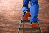 Fototapeta Do pokoju - Professional worker climbing up ladder near brick wall, closeup. Low angle view
