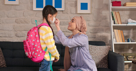 A mother wearing a turban wears a face mask for a girl who goes to school during the coronavirus or flu epidemic. Mother and child in preschool or kindergarten during the COVID 19 outbreak.