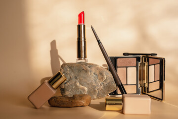 Makeup cosmetics in beige tones. Red lipstick, eye shadow, eyebrow pencil, foundation. The shadow of a plant on a beige background. Trendy cosmetics .