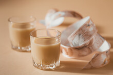Short Glasses Of Irish Cream Liquor Or Coffee Liqueur With Ribbon On A Light Beige Background