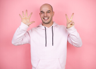 Young bald man wearing casual sweatshirt over pink isolated background showing and pointing up with fingers number seven while smiling confident and happy