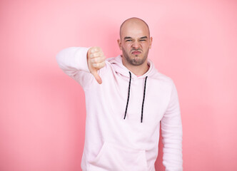 Wall Mural - Young bald man wearing casual sweatshirt over pink isolated background with angry face, negative sign showing dislike with thumb down