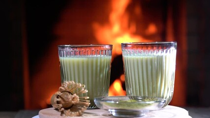 Wall Mural - Matcha green latte tea ,matcha powder and bamboo whisk on wooden board rotate before cozy burning fireplace.