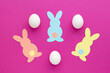 Easter bunny decoration. Paper cut DIY holiday colorful rabbits and white easter eggs .Top view,  copy space on pink  background.