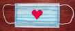 medical blue mask with red heart in the middle on wood background
