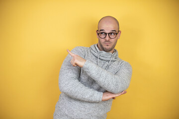 Wall Mural - Young bald man wearing glasses over yellow background pointing with hand and finger to the side