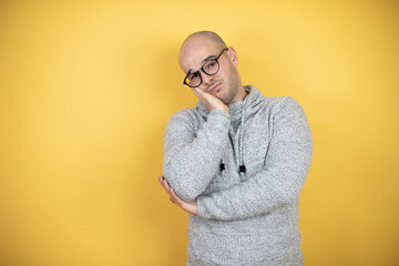 Wall Mural - Young bald man wearing glasses over yellow background thinking looking tired and bored with crossed arms