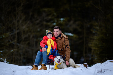  A father with a beautiful daughter and a husky dog are walking in the winter forest.