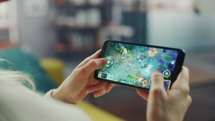 Fototapete - Close Up on Hands Playing an RPG Strategy Video Game on a Horizontally Held Smartphone at Home Living Room. Feminine Hands Tapping the Mobile Phone Screen with a Colorful Game Over the Internet.