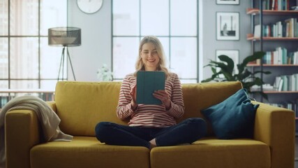 Poster - Beautiful Caucasian Female Using Tablet Computer in Stylish Living Room while Sitting on a Cozy Couch Sofa. Young Woman Resting at Home, Browsing Internet, Using Social Networks, Having Fun in Flat.