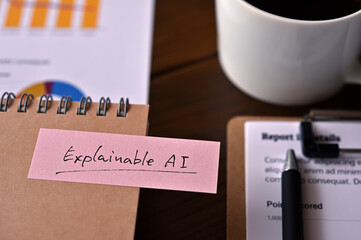 Poster - On the desk there is a laptop, a cup of coffee, and a sticky note with the word financial term Explainable AI.