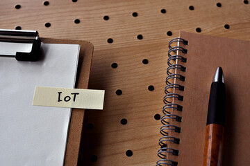 Poster - There is a notebook, a pen, and a clipboard with a sticky note stuck to it that says IoT written on it. It was an abbreviation for Internet of Things.