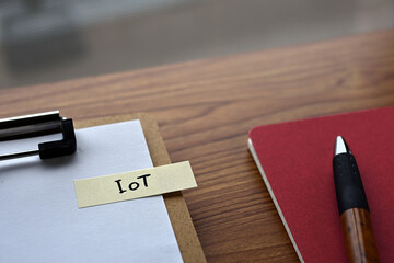 Poster - There is a notebook, a pen, and a clipboard with a sticky note stuck to it that says IoT written on it. It was an abbreviation for Internet of Things.
