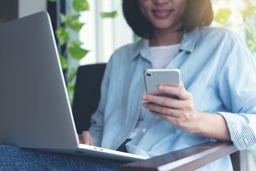 Wall Mural - Asian casual business woman, freelancer using mobile phone and online working on laptop computer in coffee shop